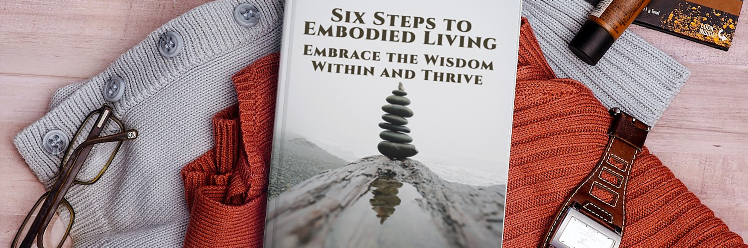 The Six Steps to Embodied Living: Embrace the Wisdom Within and Thrive e-book laying on a sweater with a pair of glasses in the corner.